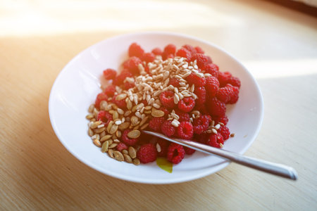 fresh red healthy raspberry with sunflower seed, white plate, wooden background
