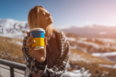 Ukrainian female drink hot coffee drink from disposable cup at nature, mountainsの写真素材