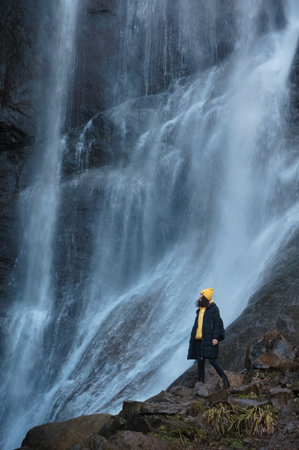 female tourist looking at waterfall in mountains outdoorsの写真素材