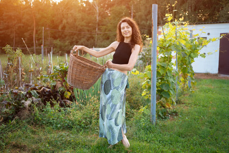 young female farmer hold wicker basket with gathering harvest at sunny gardenの写真素材