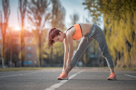 attractive brunette woman warm up and stretching in park at sunshineの写真素材