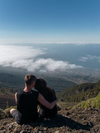 romantic lovely couple sitting on mountain top above clouds and looking on viewの写真素材