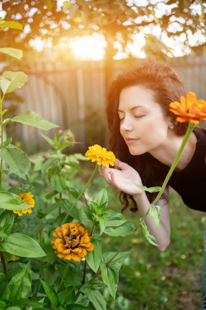pretty brunette female smelling bloom yellow flowers in garden outdoorsの写真素材