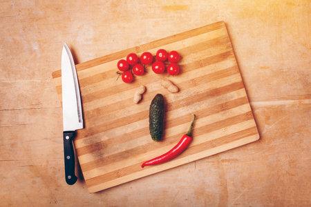 face like composition of fruits and vegetables on chopping board with knifeの写真素材
