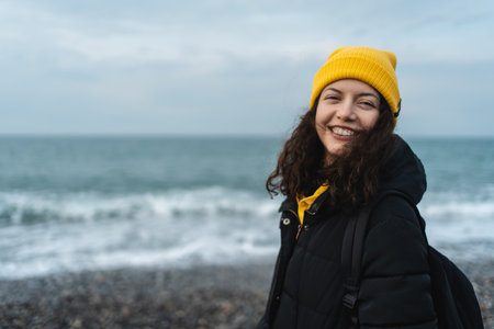 portrait of happy smiling woman walking outdoors in sea shore beach in winterの写真素材