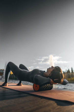 active fitness woman practicing muscular relaxation exercise with massaging foam roller, person stretching with fascial release equipment after sports training, back pain and body stiffness releaseの写真素材