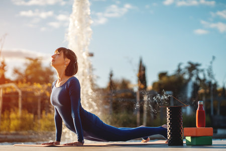 young woman practicing yoga at sunset outdoors, body conscious person exercising stretching with foam roller, blocks, scented sticks and other accessories, balance and harmony conceptの写真素材