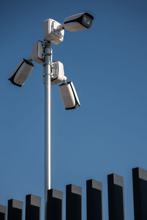 Security cameras mounted on pole monitoring surroundings in clear blue sky, video surveillance in...