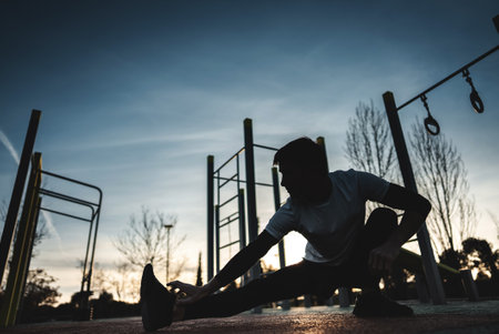 young athletic man exercising at fitness calisthenics workout and stretching legs at street gym during sunset, body improvement and strength training conceptの写真素材