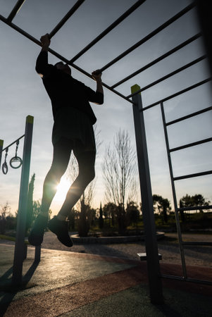 young athletic man exercising at fitness calisthenics workout and making pull-ups at street gym...