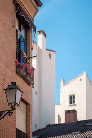 Bright balcony adorned with flowers is situated on a historic brick building, contrasting with nearby white structures under a clear blue sky in a lively urban setting.の写真素材