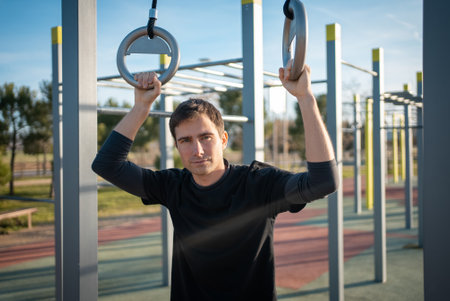 young athletic man resting after fitness calisthenics workout at street gym during sunset, taking a break during body improvement and strength trainingの写真素材