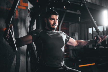 Male bodybuilder performing cable crossover for chest muscles in gym, Man training pectorals with...
