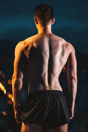 Muscular athlete with perfect physique posing from back at night, strength and dedication, Toned man...