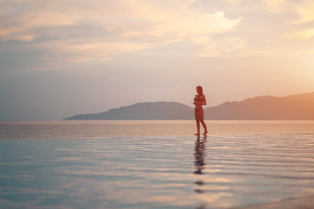 beautiful girl walking by pool flowing into sea at sunrise, serene elegance and morning peace, stunning female strolling near ocean edge at sunset or sunriseの写真素材