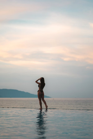 beautiful girl walking by pool flowing into sea at sunrise, serene elegance and morning peace, stunning female strolling near ocean edge at sunset or sunriseの写真素材
