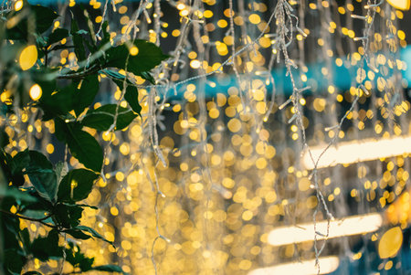 festive blurred lights with green leaves, golden holiday glow defocused through foliage background,...