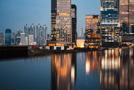 big city skyline at sunset with mirrored water reflection, modern high-rise skyscrapers at golden...