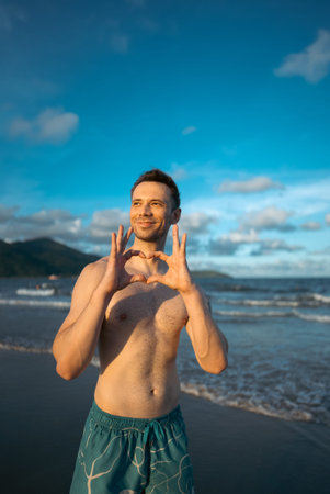 handsome white man with athletic muscular body standing at beach at sunny sunset, attractive male...