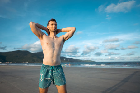 handsome white man with athletic muscular body standing at beach at sunny sunset, attractive male athlete walking at sea or ocean shoreの写真素材