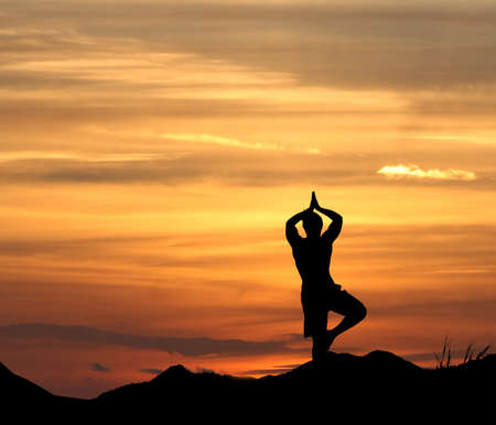 Young man practices yoga on mountain with sunsetの写真素材
