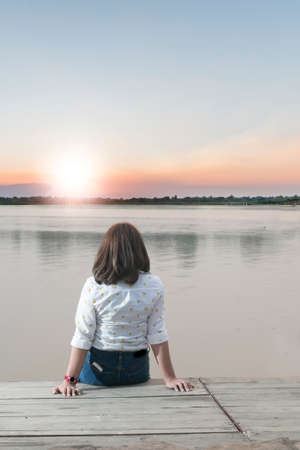 Lonely girl looking sunset at river sideの写真素材