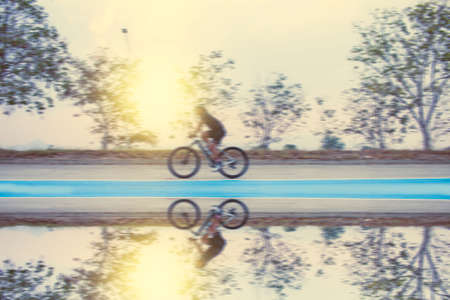 Blurry young man bicycle on the road with reflectionの写真素材