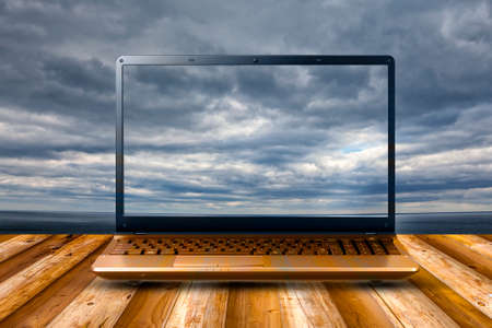 Laptop on wooden table with cloud sky backgroundの写真素材