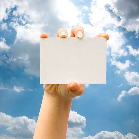 Hand holding blank paper business card on blue sky backgroundの写真素材