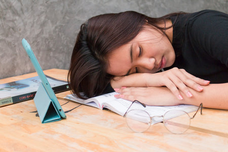 Tired student asian girl sleeping on book with tablet in coffee shop, Resting studentの写真素材