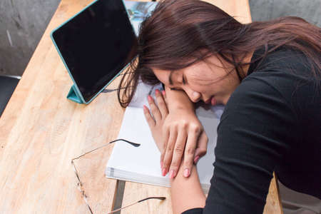 Female asian student sleeping on book with tablet  in cafe,Tired of studying. Top viewの写真素材