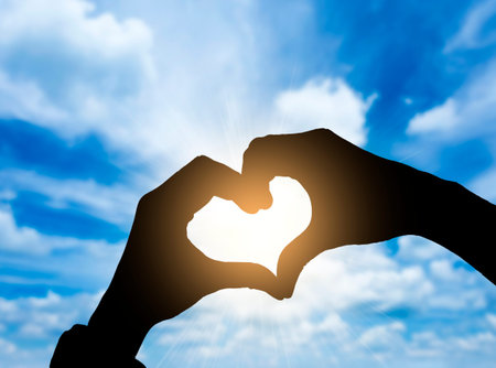 Heart shape hand gesture with blue skyの写真素材