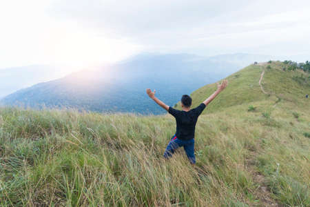 Happy young man standing with raised arms in mountainsの写真素材