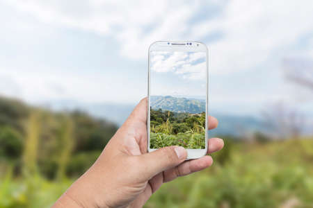 Male hand using smart phone with take photo at beautiful moutain in Thailandの写真素材