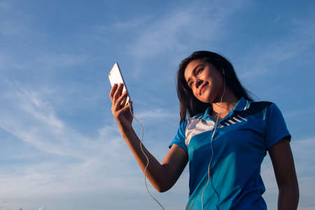 young smiling asian girl take photo with mobile phone outdoor shotの写真素材