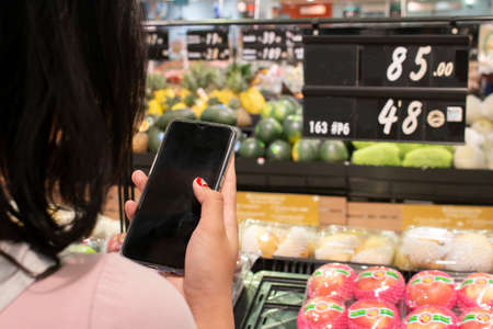 Woman using mobile phone while shopping in supermarketの写真素材