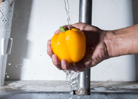 Bell chilli pepper on male hand with water splashの写真素材