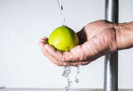 Fresh lemon on male hand cleaning with falling waterの写真素材