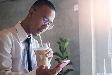 Young business man drinking ice coffee and using phoneの写真素材
