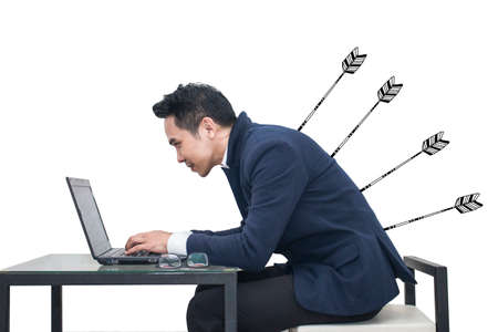 Asian Businessman sitting at a desk using a laptop with arrow stabbing his back,Business conceptの写真素材