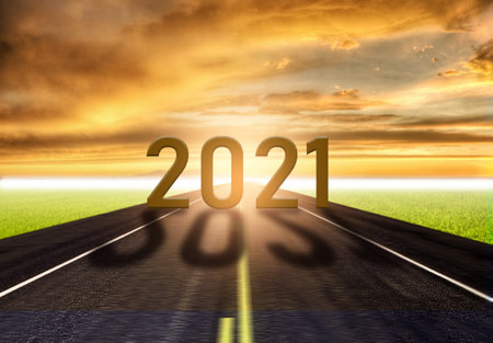 The word 2021 on empty asphalt road at golden sunset and beautiful blue sky. Concept for  year 2021.の写真素材
