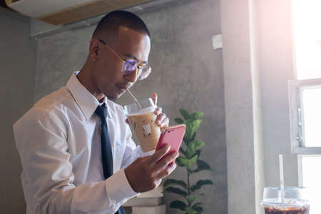 Young business man drinking ice coffee and using phoneの写真素材
