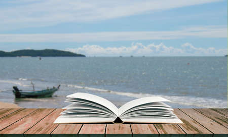 Open book on wooden table with blurred sea backgroundの写真素材