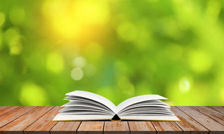 Open book on wooden table with blurred trees backgroundの写真素材