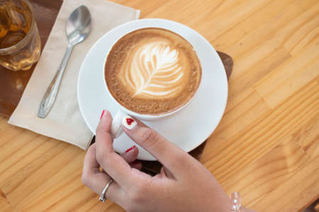 Top view women hand with latte coffee on wood tableの写真素材