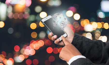 man holding a phone with 5G holograms on city background. 5G network concept, high speed mobile internet, mixed media new generation network.の写真素材