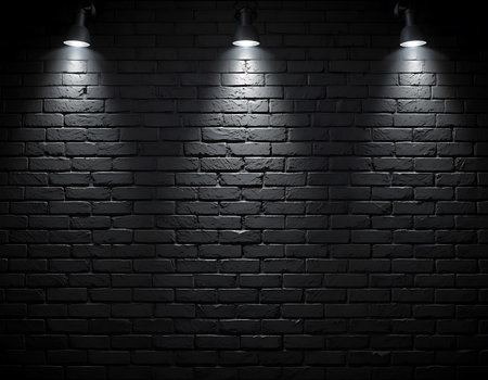Dark black brick wall illuminated by three focused spotlights, creating a dramatic and moody atmosphere, ideal for design, stage, or presentation backgroundsの素材