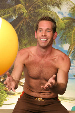guy on the beach in swim trunks throwing a beach ball at youの写真素材