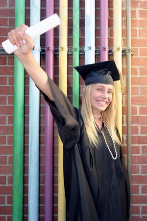 Young Girl in her cap and gown graduates smiling she holds up her diploma in front of colorful backgroundの写真素材