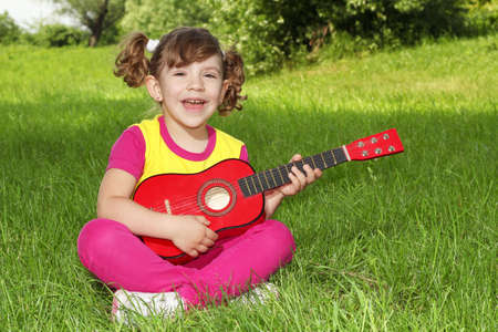 little girl sitting on grass play guitar and singの写真素材